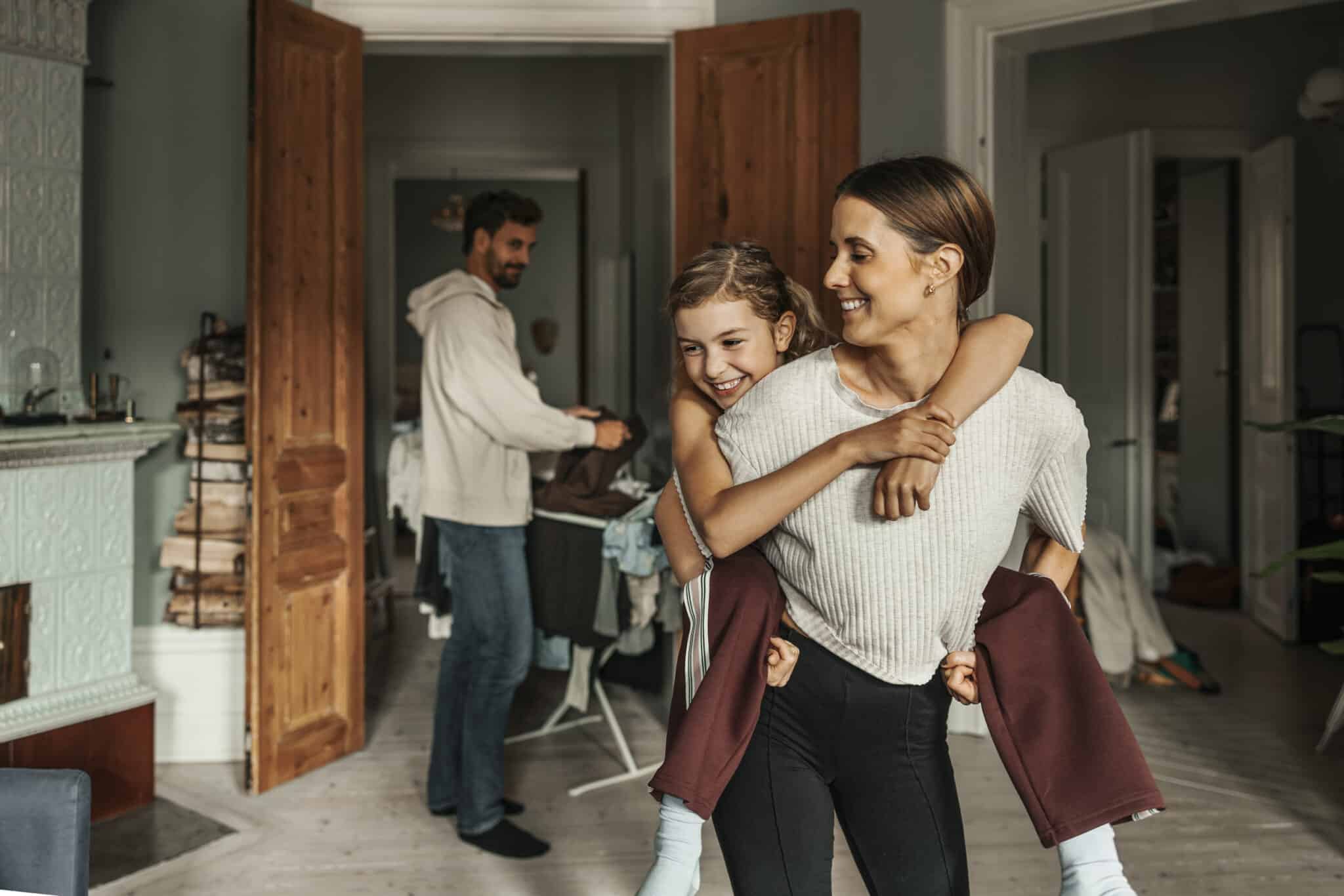 Smiling mother piggybacking her daughter at home